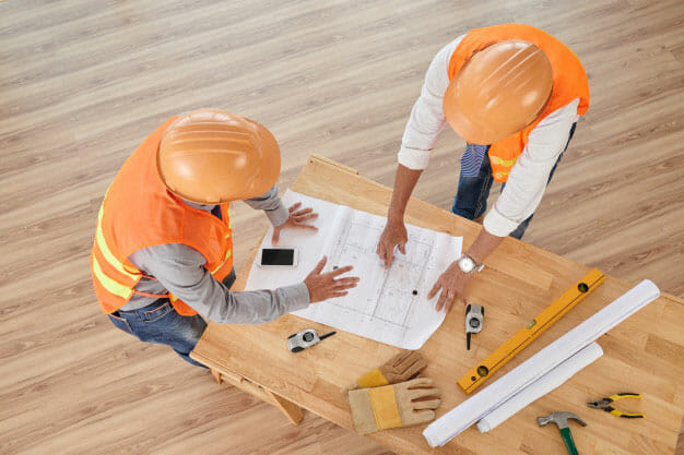two contractors at construction table studying blueprint